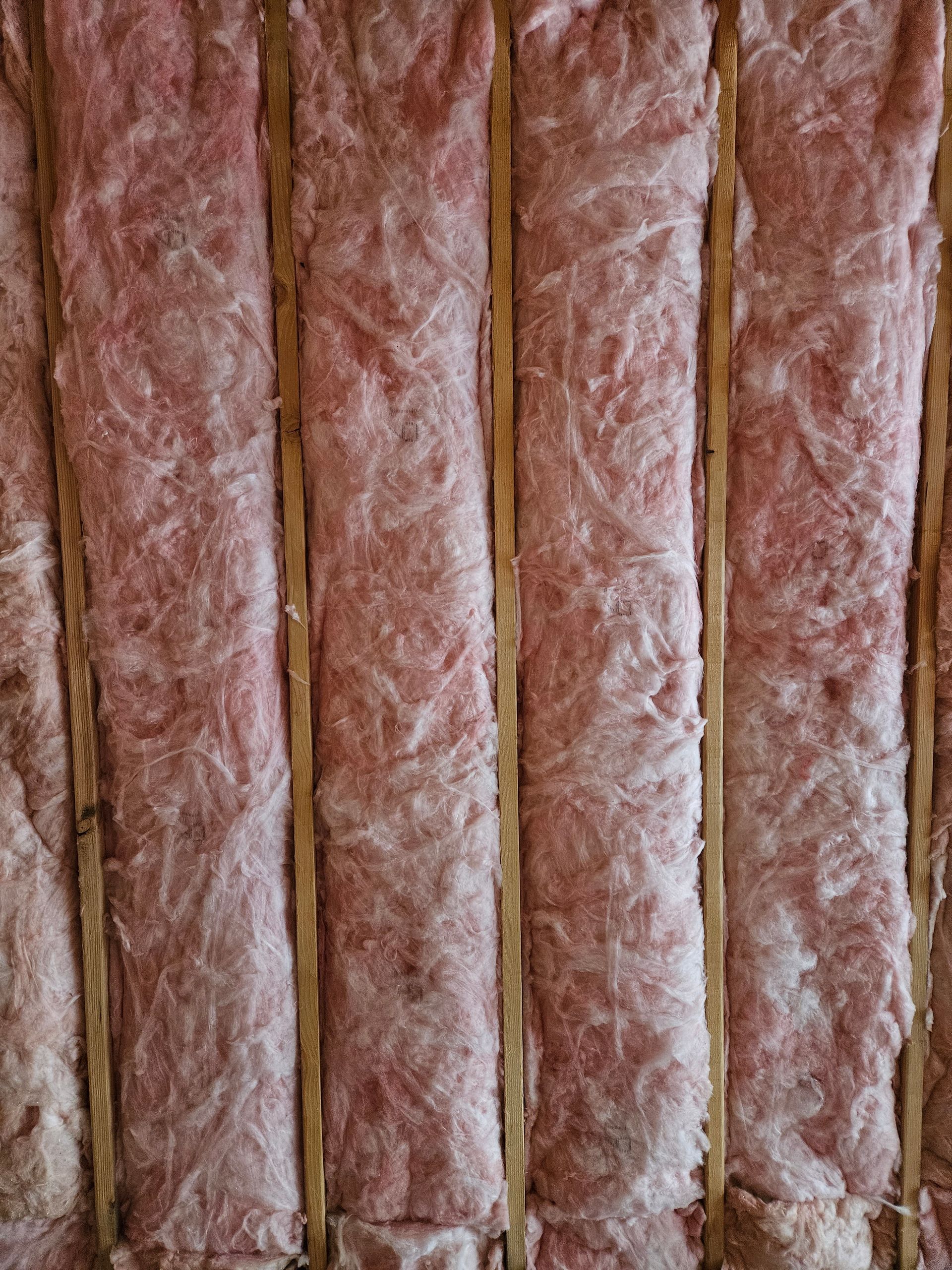A close up of a wall with pink insulation and wooden beams.