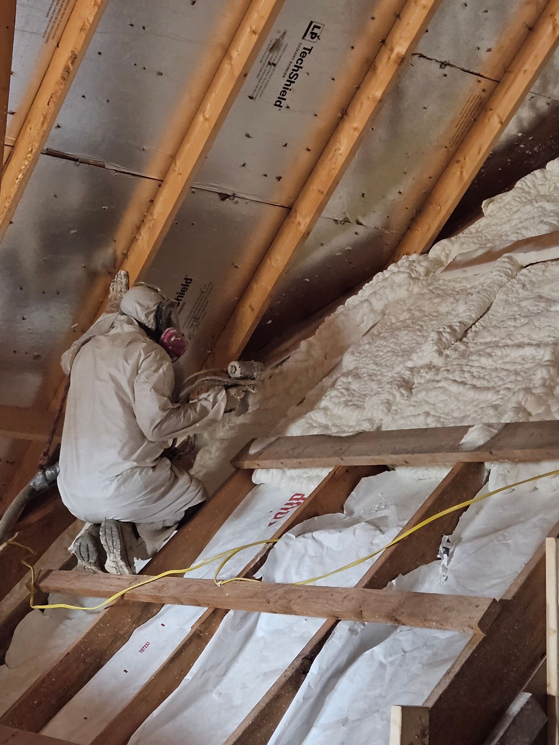 A man is spraying insulation on the roof of a building.