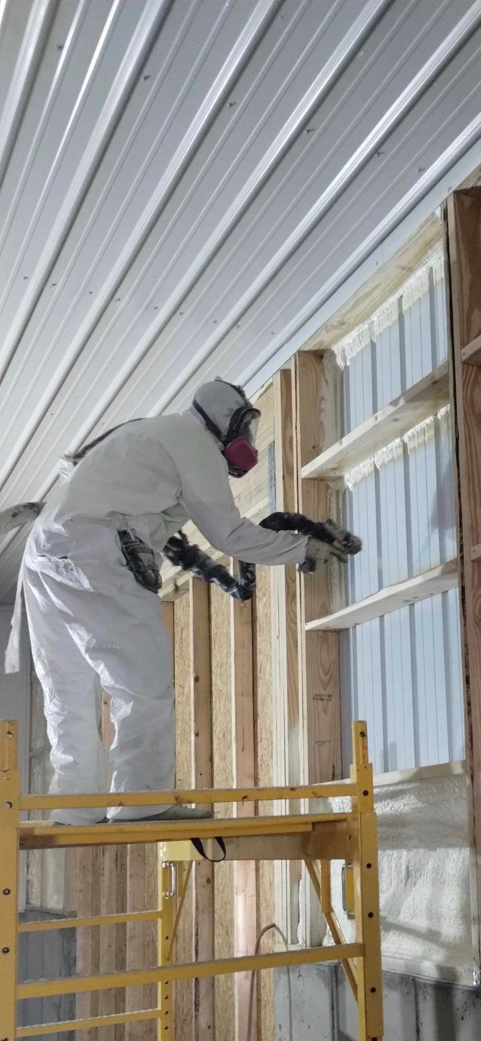 A man spraying insulation on a wall while on scaffolding.