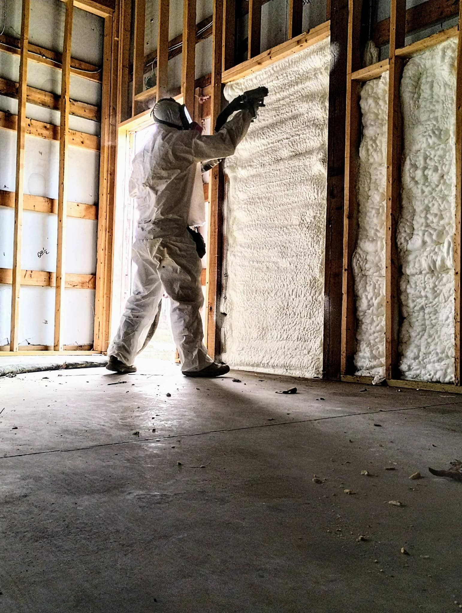 A man in a protective suit spraying insulation on a wall.