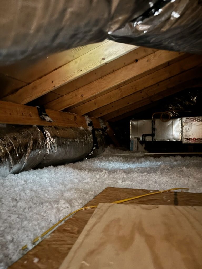 There is a duct in the attic with insulation and a measuring tape.