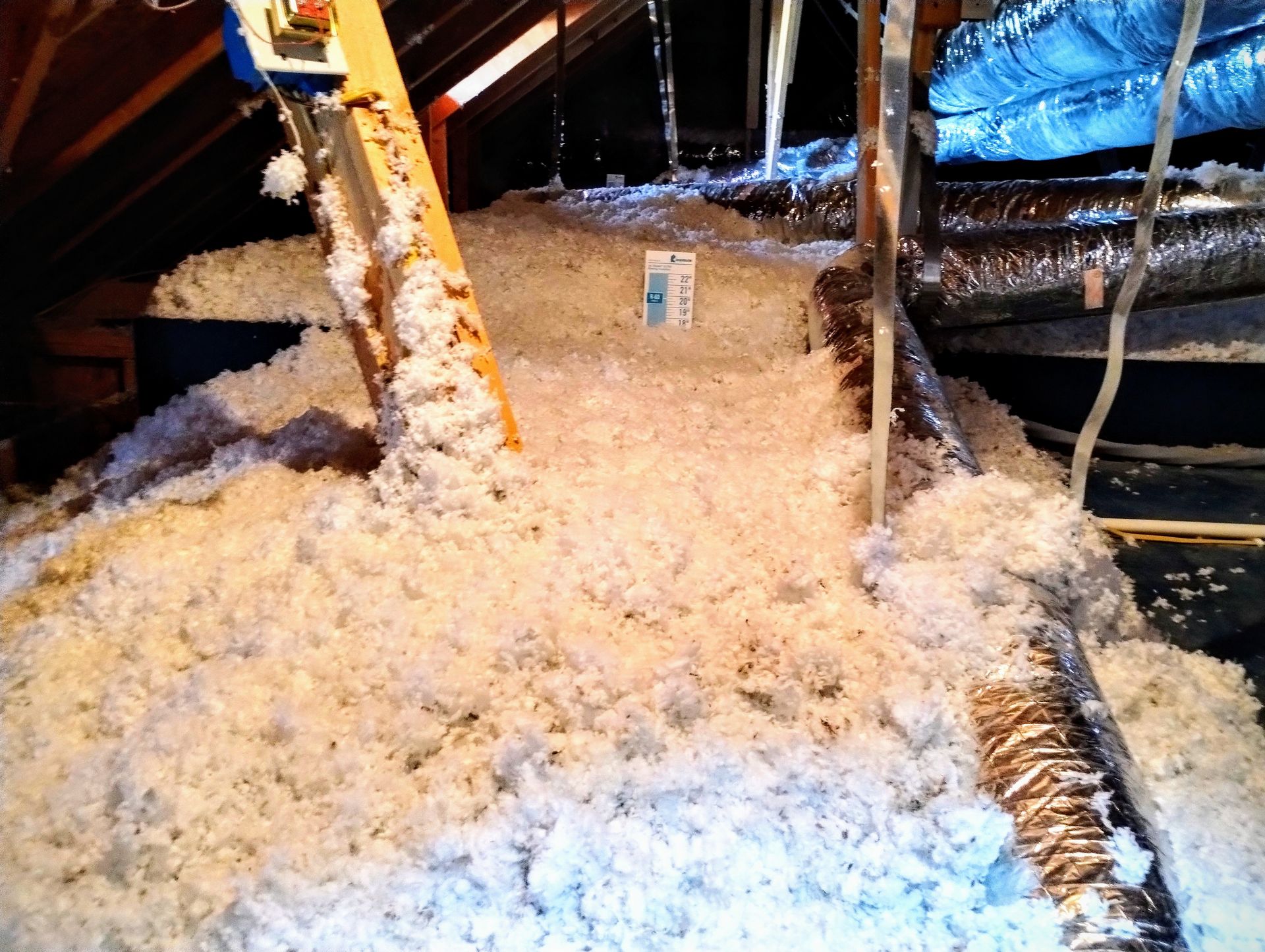 A pile of insulation in an attic with a ladder in the background.